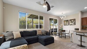 A spacious living area with a sectional sofa, a dining table with chairs, and a kitchen area with a bar counter. - Relaxed Island Living- WD, AC, Backyard, Workspace (Ewa Beach)