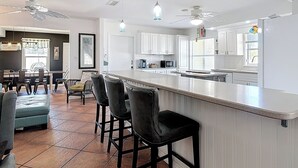 Una cocina moderna con armarios blancos, una isla central con taburetes altos e iluminación colgante.