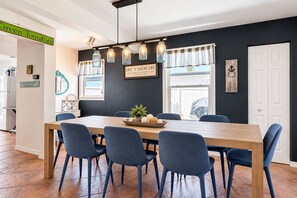 Un coin repas avec une table en bois, des chaises bleues et un saladier rempli de fruits.