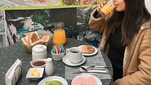 Una mesa de comedor con un montaje de comida que incluye pan, una jarra de jugo de naranja, una taza de café y platos de comida.