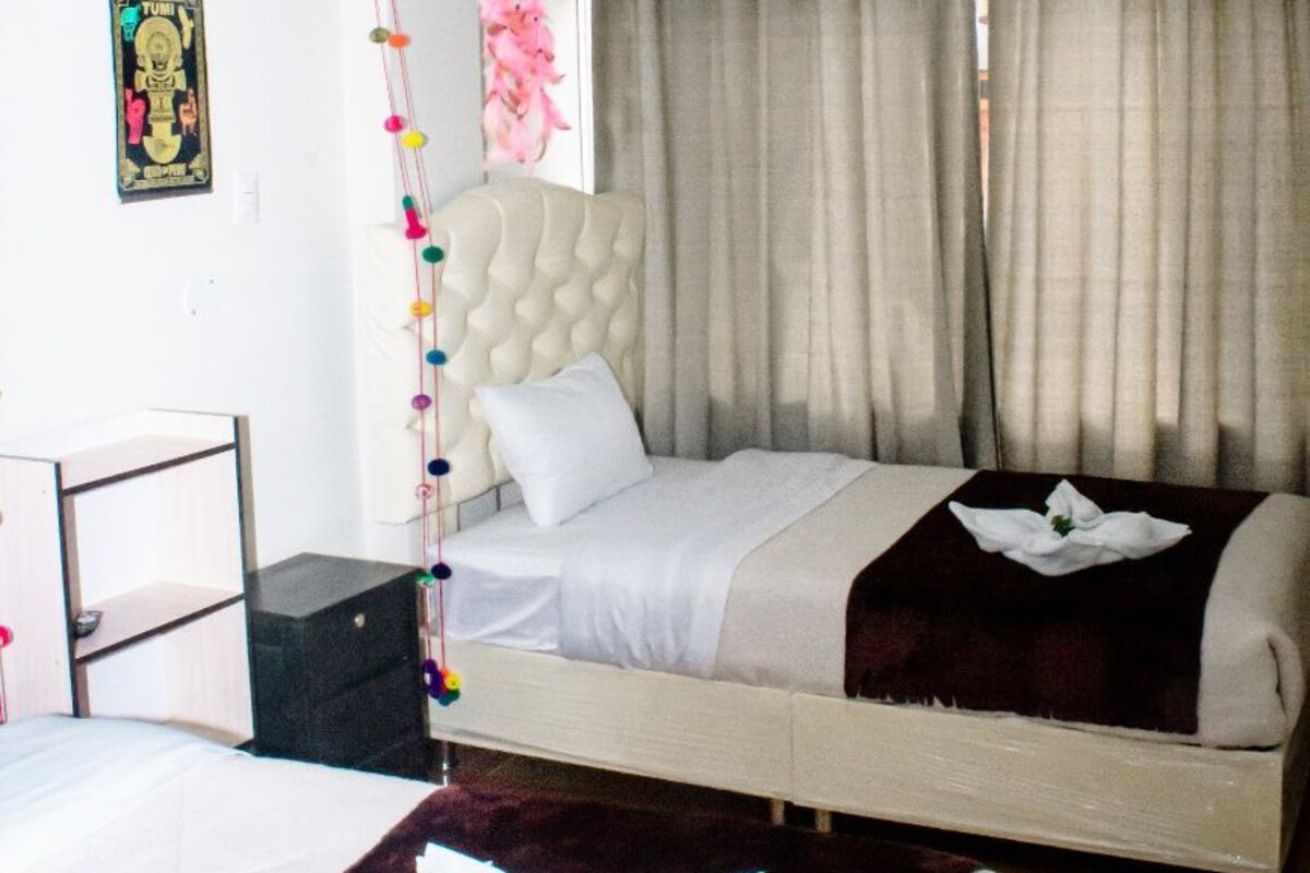 Habitación de hotel con una cama, un escritorio y una silla. Hay una cortina en la ventana y un adorno en la pared.