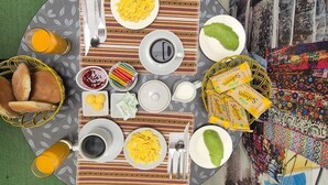 Una mesa redonda de comedor con platos de huevos revueltos, tostadas y una ensalada verde, rodeada de sillas.