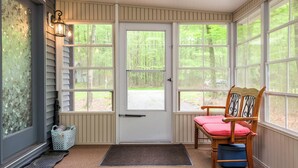 A sunroom with a large door, a chair with a cushion, and a basket on the floor.