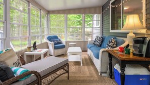A cozy room with a large window, a sofa, a chair, a small table, and a lamp.