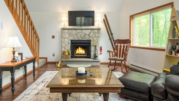 A living room with a stone fireplace, wooden staircase, leather sofa, and a large window.