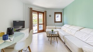 A modern living room with a glass dining table, white sofa, and a television on a stand.