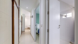 A hallway leading to a bedroom with a bed, a desk, and a chair.