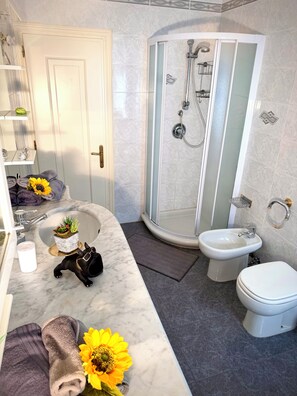 Un baño con lavamanos de mármol, un bidé, inodoro y cabina de ducha.