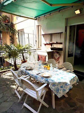 Un área de comedor al aire libre con una mesa dispuesta para dos personas, rodeada de sillas blancas, bajo un dosel verde.