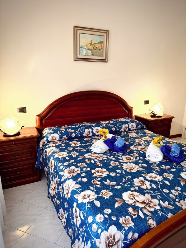 Una cama con colcha floral, dos mesitas de noche con lámparas, un cabecero de madera y un cuadro en la pared.