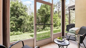 A balcony with a glass door, a table with a plate of fruit and glasses, and a grill set up outside. - Disney Charm, Steps From Pool and Clubhouse! (Kissimmee)