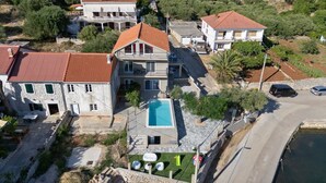 Un quartier résidentiel avec une grande maison dotée d’une piscine, d’une façade en pierre et d’un toit recouvert de tuiles rouges.
