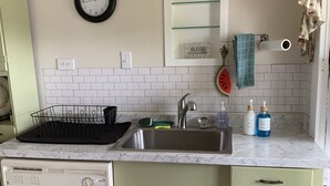Una cocina con salpicadero de azulejos blancos, un fregadero, lavavajillas y armarios verdes.