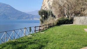 A grassy area with a metal fence, a stone wall, and a paved path. - Peaceful Lakefront (Vello)