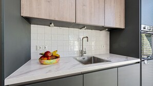 A modern kitchen with wooden cabinets, a stainless steel sink, and a bowl of fruit on the countertop.