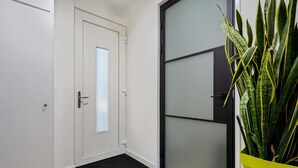 A hallway with a white door, a black-framed glass door, and a green plant in a yellow pot.