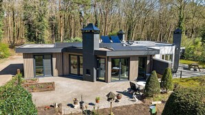 A modern house with large glass windows, a patio with outdoor furniture, and a garden area with potted plants.