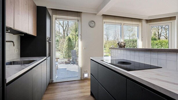 A modern kitchen with a built-in oven, a sink, and a window with blinds.