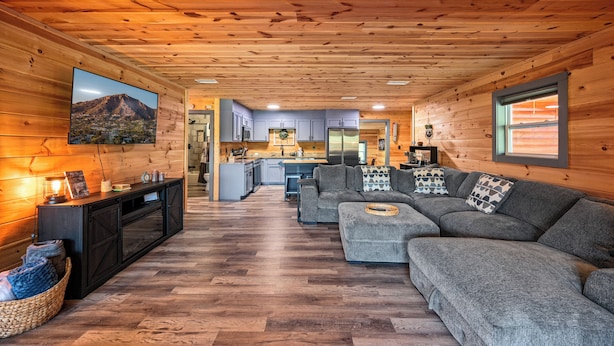 Un interno accogliente con zona giorno che presenta un divano modulare grigio, soffitto in legno e una cucina sullo sfondo.