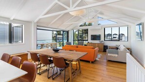 Amplia sala de estar con mesa de comedor de madera, sofá naranja y televisor montado en la pared.