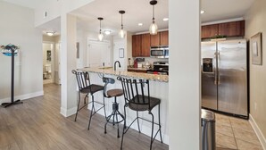 Une cuisine moderne dotée d’un îlot central, d’appareils électroménagers en acier inoxydable et de luminaires suspendus.