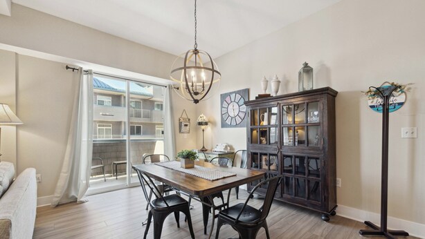 Un coin repas avec une table en bois, des chaises noires et un lustre. On y trouve également un meuble avec des portes en verre, sur lequel sont disposés des objets décoratifs.