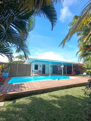A backyard with a swimming pool, a covered patio, and a wooden deck.