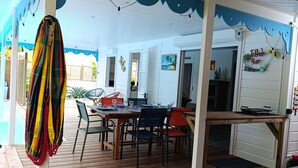 Un área de comedor al aire libre con techo, una mesa y sillas de madera, un paraguas colorido y vistas a la piscina.