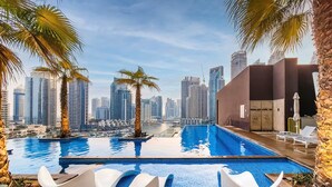 Zona de piscina con sillas modernas, palmeras y el perfil urbano del fondo.