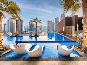 Area piscina con moderne sedie, palme e uno skyline cittadino sullo sfondo.