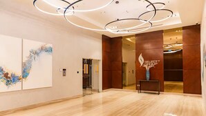 Un lobby moderno con piso de mármol, arte abstracto en la pared y un mostrador de recepción. Se observa un logotipo en la pared.