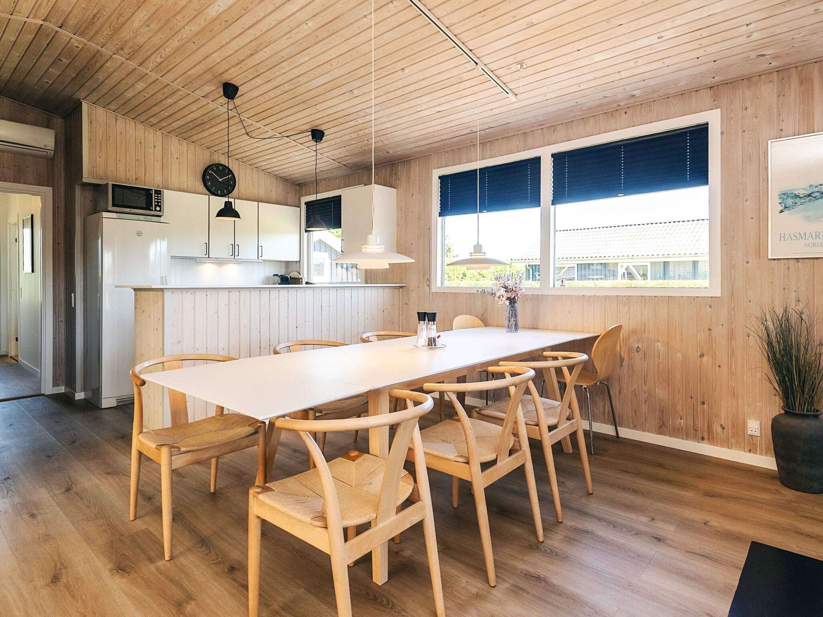 Una cocina moderna con armarios de madera, encimera blanca y comedor con una mesa larga y sillas.