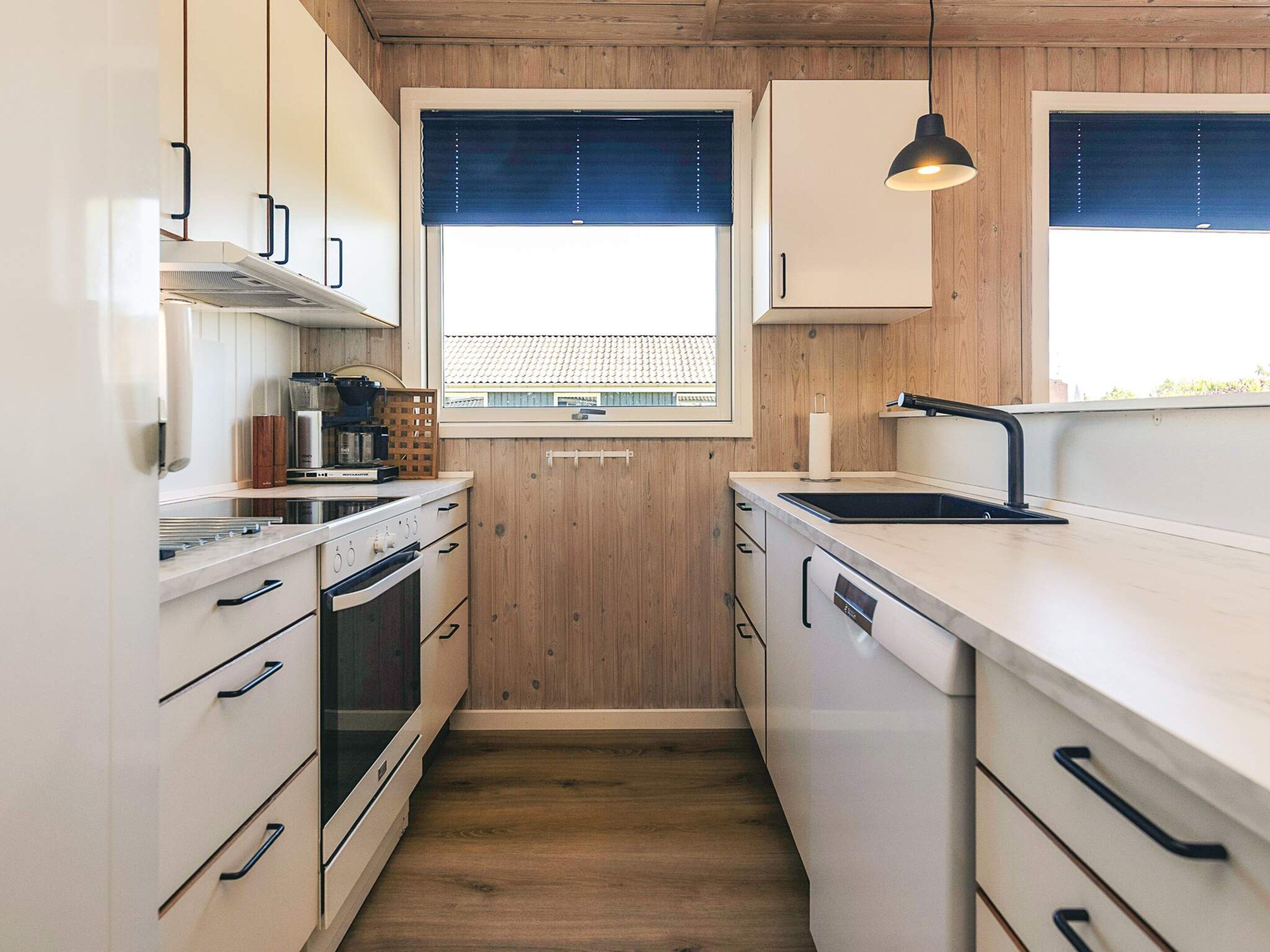 A modern kitchen with wooden cabinets, a built-in oven, a sink, and pendant lighting.