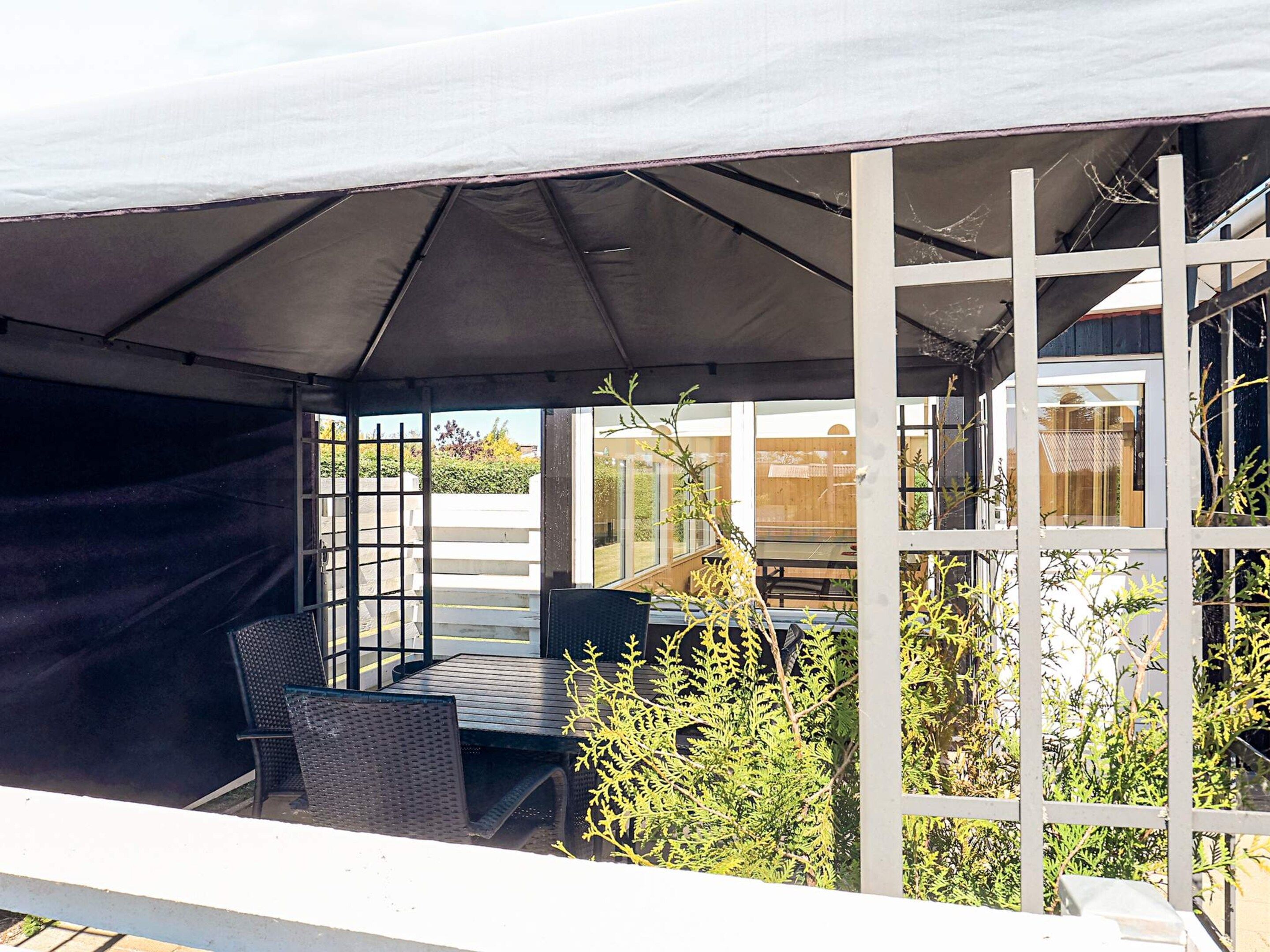 Une terrasse extérieure avec une table et des chaises, un espace abrité et une vue sur un bâtiment en arrière-plan.