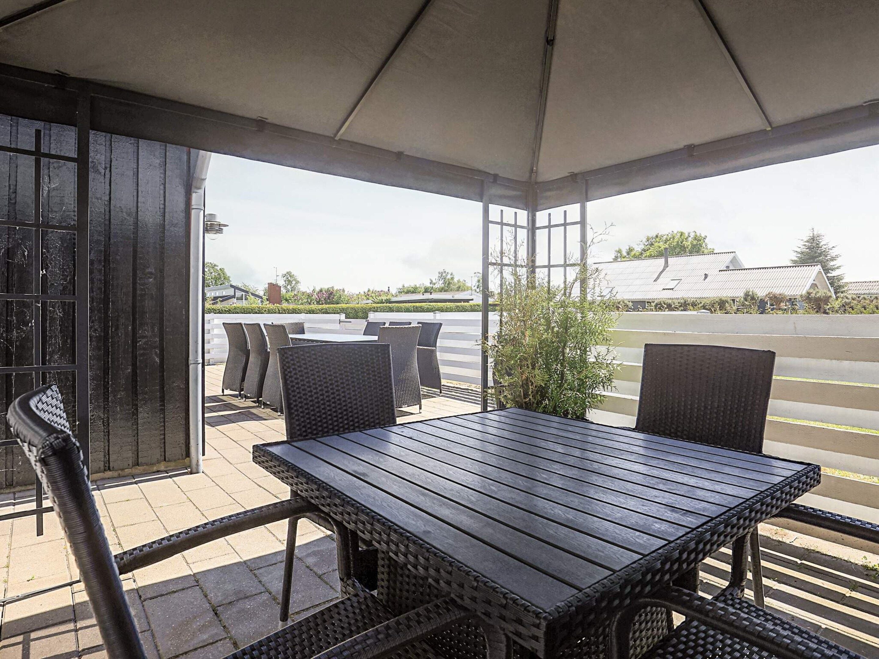 An outdoor patio with a table and chairs, a covered area, and a view of a parking lot and buildings.