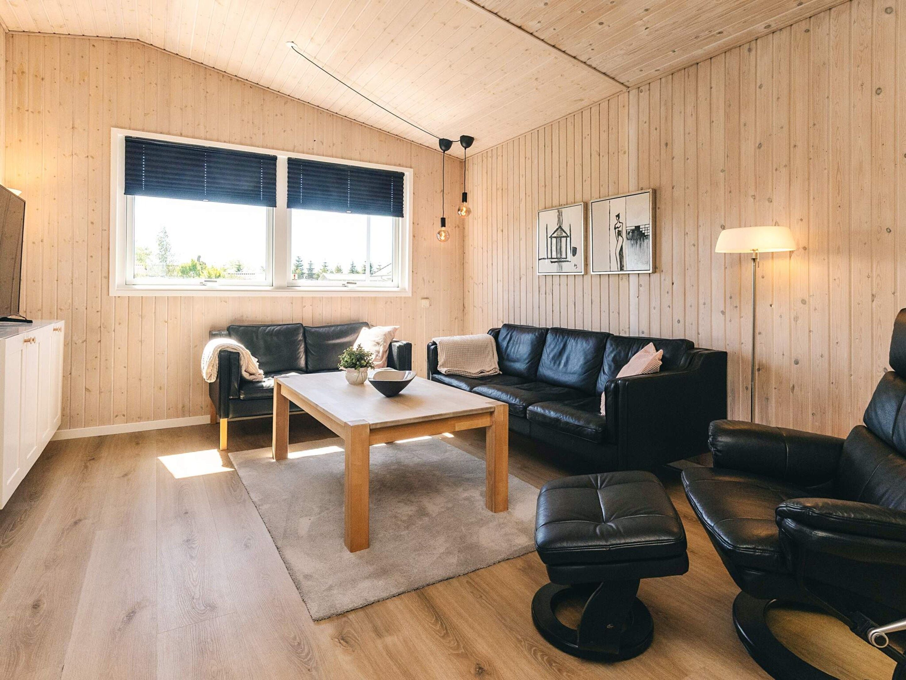 Una sala de estar acogedora con techo de madera, un sofá de cuero negro, una mesa de centro de madera y un reposapiés de cuero negro.
