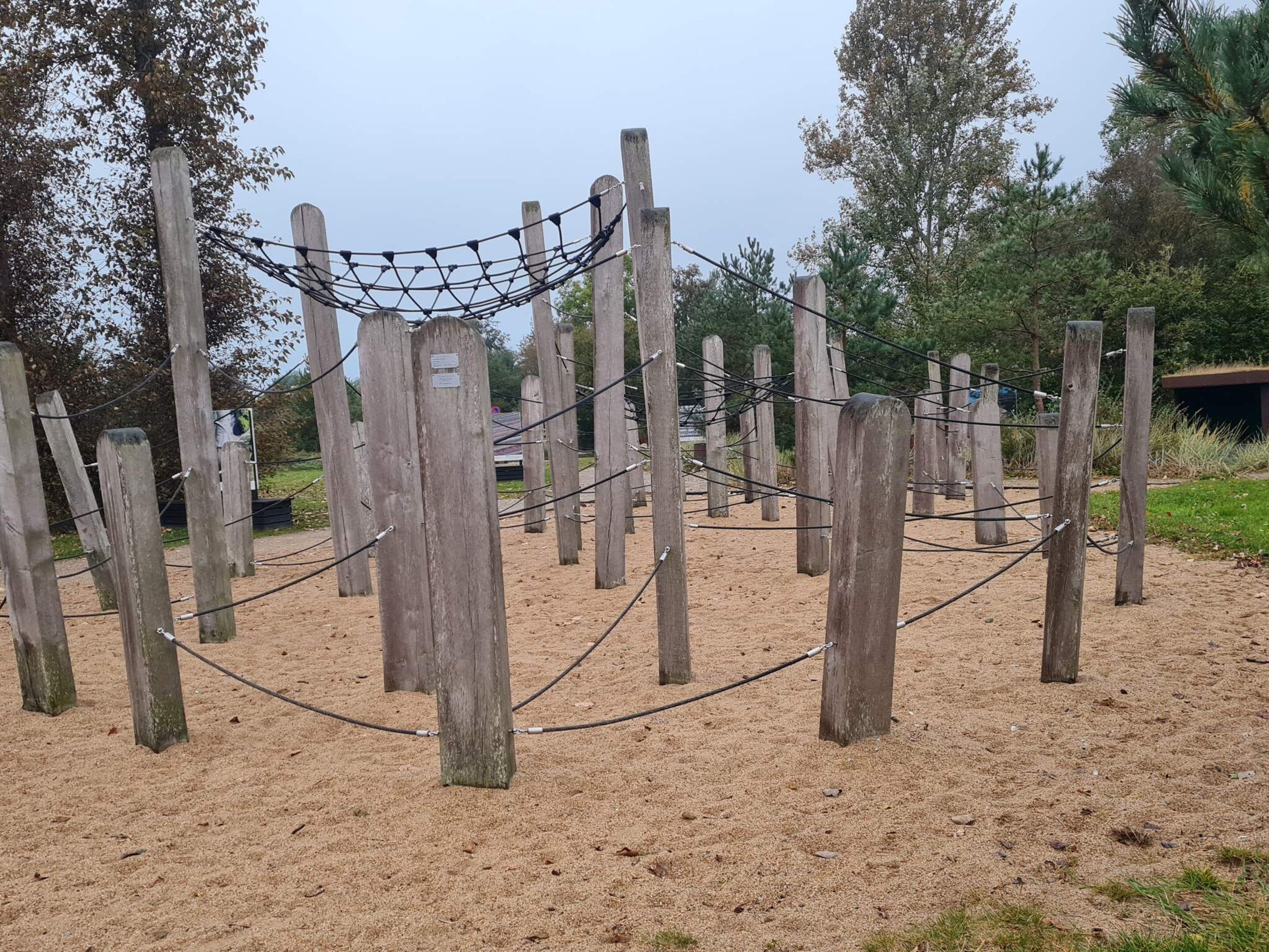 A wooden fence with a rope barrier in a sandy area, surrounded by trees.