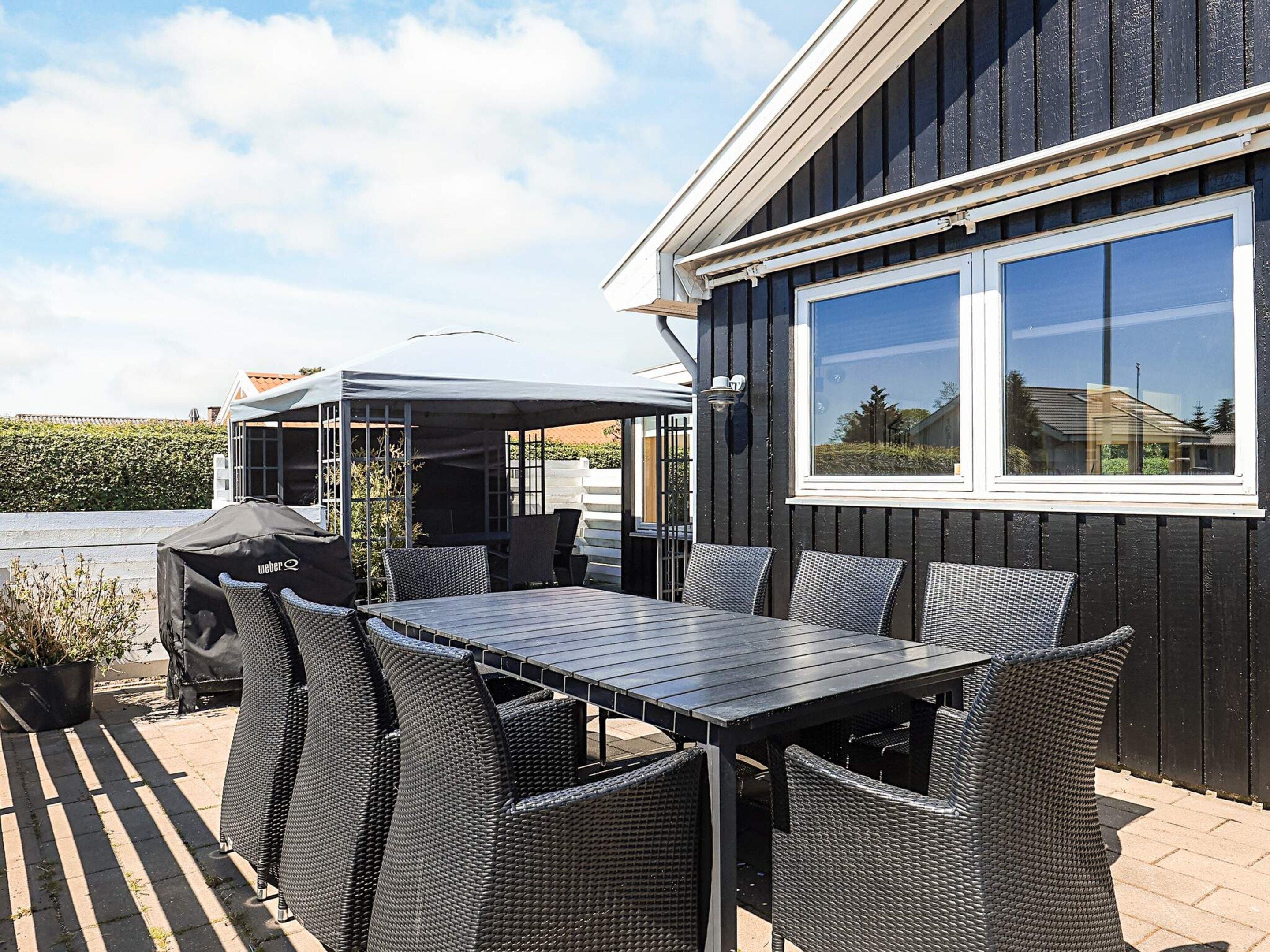 Un patio exterior con mesa y sillas, un área de estar cubierta y vistas a un edificio residencial.