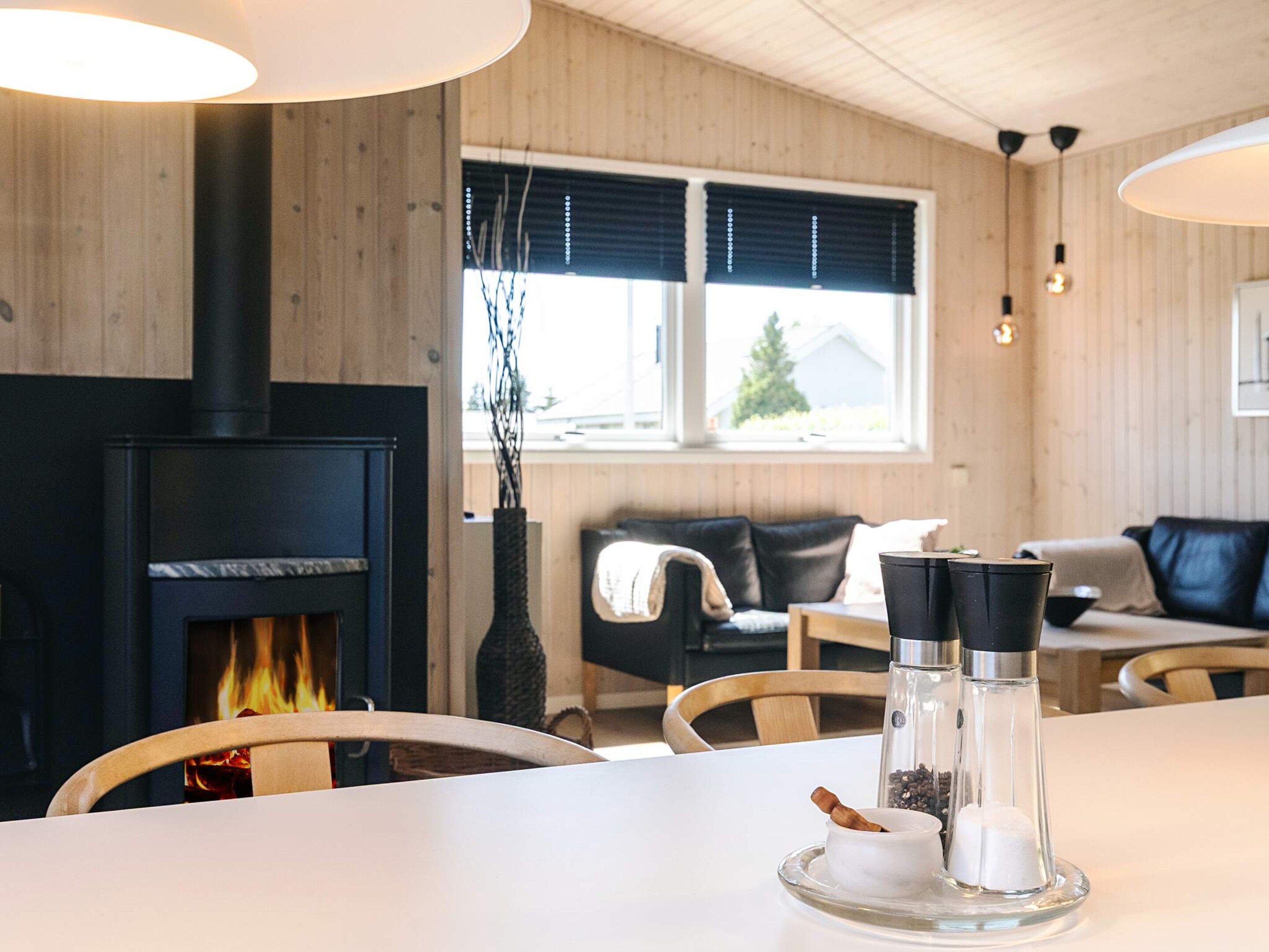 Una sala de estar moderna con chimenea, paredes de madera, un sofá y una mesa de comedor con saleros y pimenteros.