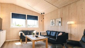 A cozy living room with a wooden floor, two black leather sofas, a wooden coffee table, and a large window with blinds.