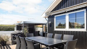 An outdoor patio with a table and chairs, a covered seating area, and a view of a residential building.