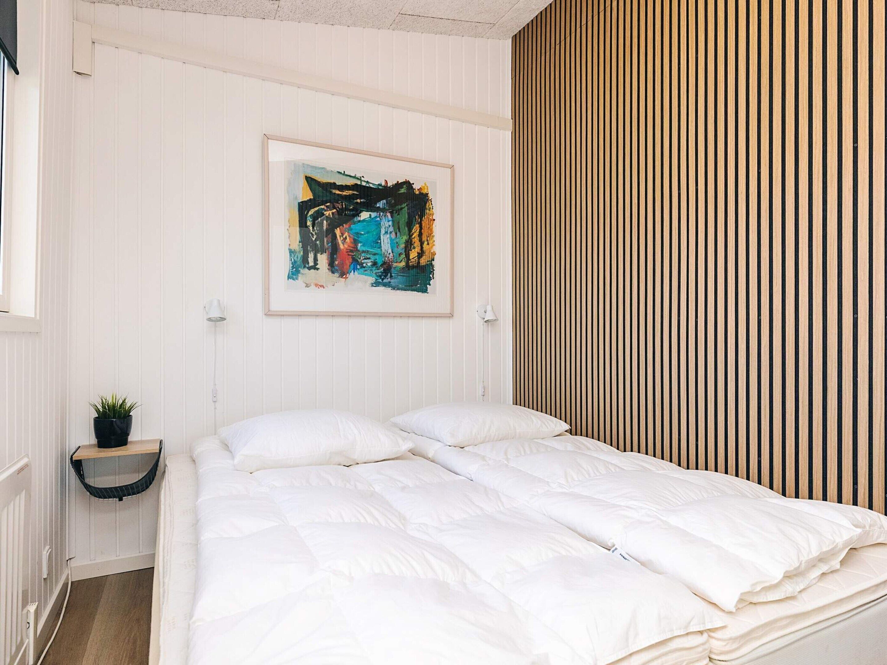 Ein ordentlich gemachtes Bett mit weißer Bettwäsche, ein gerahmtes abstraktes Gemälde an der Wand und ein vertikal gestreiftes Muster auf der rechten Wand.