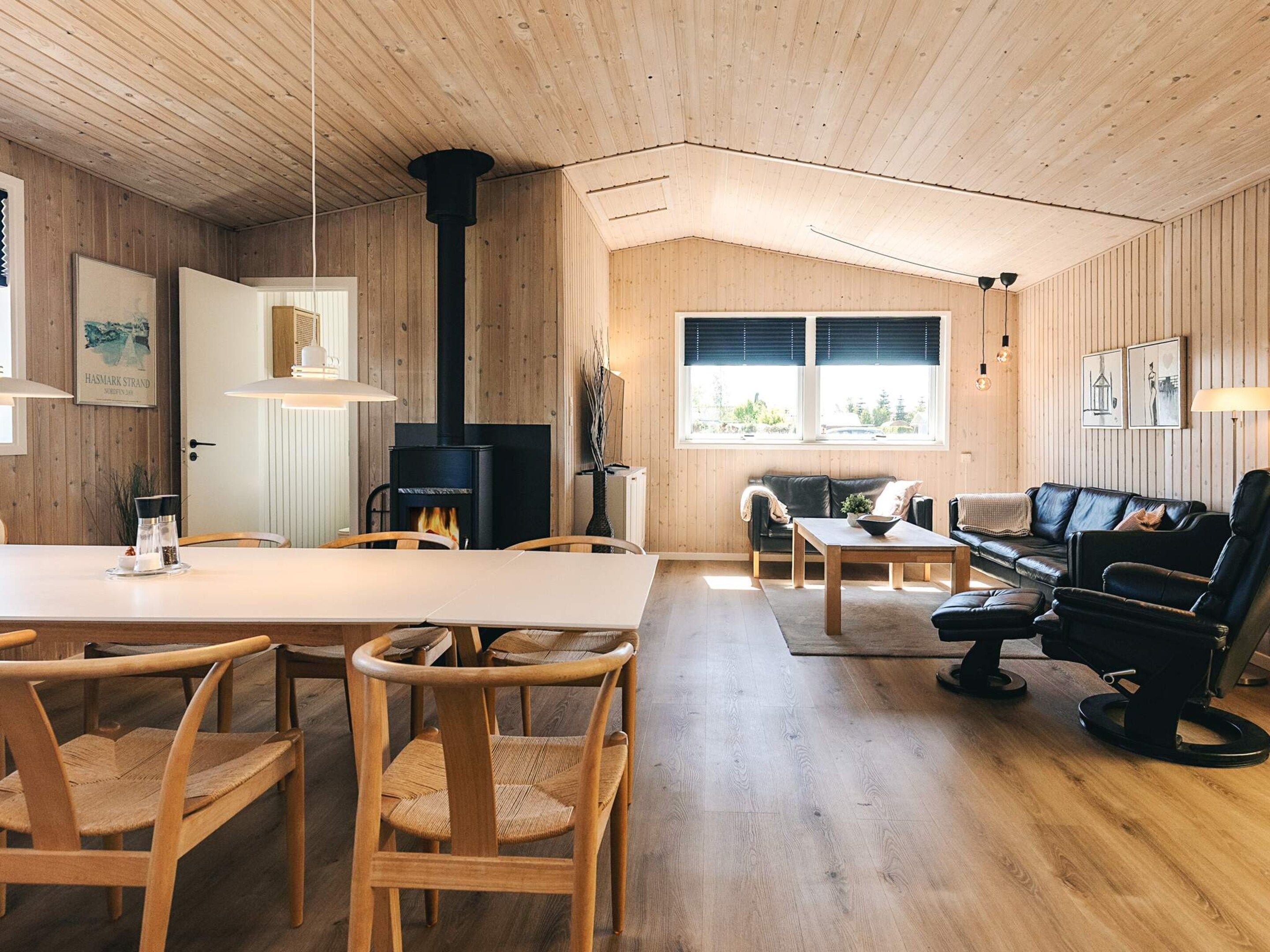Una sala de estar acogedora con chimenea, paredes de madera, una zona de comedor con sillas y un sofá.