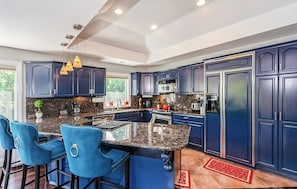 Een moderne keuken met donkerblauwe kastjes, een granieten aanrechtblad en een centraal eiland met barkrukken.