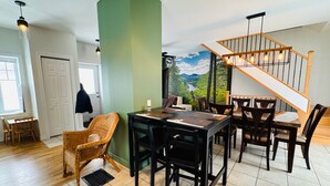 Un espace repas offrant une vue sur une forêt et des montagnes, un escalier et une porte donnant sur une autre pièce.