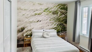 Une chambre à coucher avec un lit, une table de chevet, une lampe et une fresque murale représentant des palmiers.
