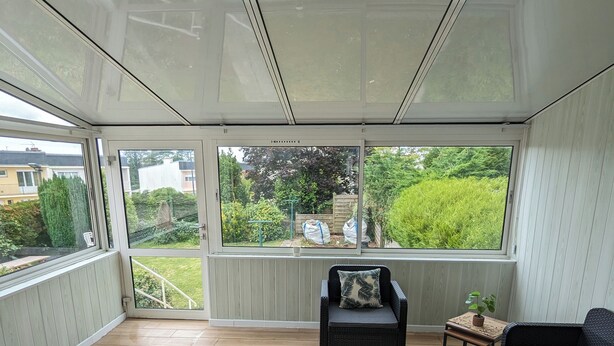 A covered patio area with a view of the garden, furnished with a sofa, armchair, and coffee table.