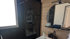 A modern bathroom with a black marble shower, a white sink, and a wooden vanity.