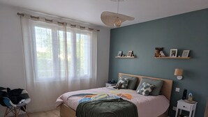A bedroom with a bed, a nightstand, a chair, a window with curtains, and a wall with shelves.