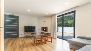 A modern living room with a wooden floor, a flat-screen TV, a fireplace, and a large sliding glass door leading to an outdoor area. - Villa Lorenzo by Atlantic Holiday (São Vicente)